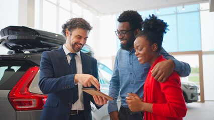 Professional auto dealer talking with potential buyers in car showroom. Man showing car...