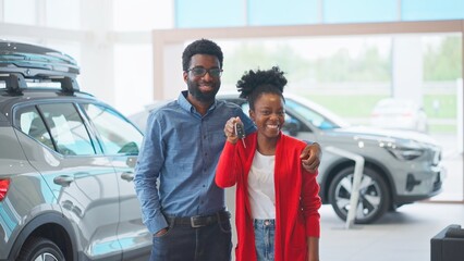 Camera view of African American couple standing in middle of auto salon. Satisfied husband hugging...