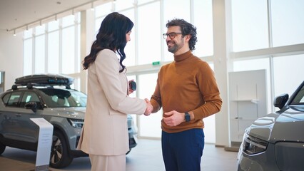 Handsome man having positive conversation with his auto dealer in auto showroom. Caucasian people cheerfully smiling to each other after successful purchase. Buying new car in auto salon.