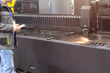 A worker operates a steel laser cutting machine at a factory