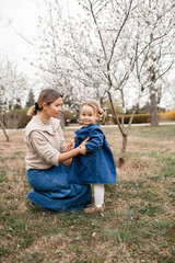 Fototapeta premium Stylish mother holding baby 1-2 year old girl wearing denim clothes outdoors. Springtime.