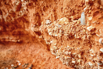 Close-up View of a Textured Orange Clay Wall With Pebbles and Natural Features in Sunlight