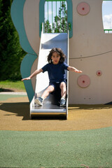 Happy child sliding down playground slide in summer