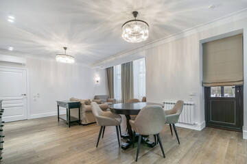 Elegant interior of the living room in pastel colors. Upholstered furniture, dark wood dining table, beautiful chandeliers.