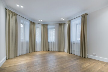An empty room with a bay window. White wall and ceiling decor, parquet, spotlights .Windows with elegant curtains.
