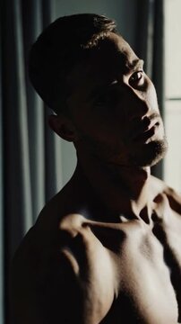 Man poses in low light highlighting muscular physique and strong profile in a serene setting