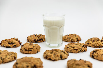 Glass of milk surrounded by oatmeal raisin cookies on a white surface. Minimal and nostalgic snack concept. Food pattern, pattern of cookies, 
