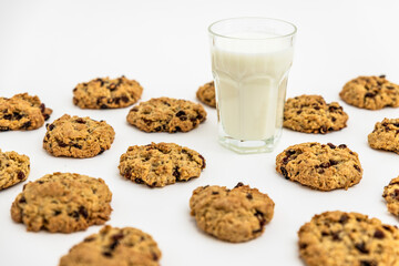 Glass of milk surrounded by oatmeal raisin cookies on a white surface. Minimal and nostalgic snack concept. Food pattern, pattern of cookies, 