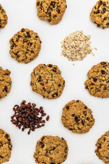 Flat lay of oatmeal raisin cookies with scattered oats and raisins on a white background. Ingredients and baked goods styled together. food pattern texture