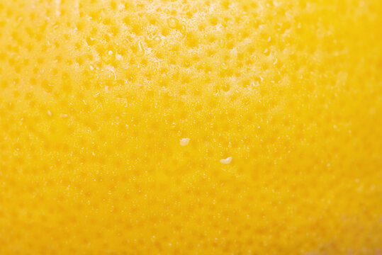Lemon with water drops macro photo as background. Lemon skin is yellow, thin focus part.