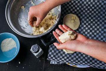 Close-up image showcasing hands taking arepa (colombian food) dough from pot with utensils, portraying culinary preparation.