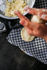 Close-up image showcasing hands forming arepa (colombian food) dough with bowls and utensils, portraying culinary preparation. Focus on background.