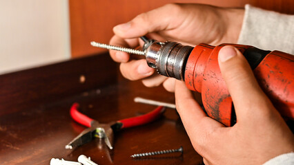 Hands holding a red power drill changing its bit on a wooden surface with other construction tools, emphasizing construction, DIY, and repair activities.