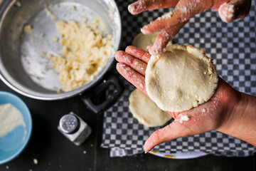 Close-up image showcasing hands forming arepa (colombian food) dough with bowls and utensils, portraying culinary preparation. Focus on background.
