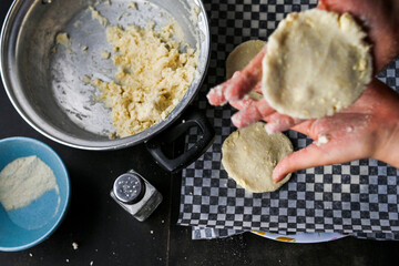 Close-up image showcasing hands forming arepa (colombian food) dough with bowls and utensils, portraying culinary preparation. Focus on background.