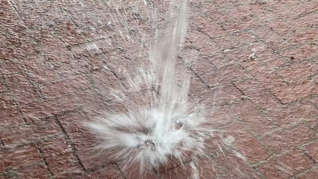A dynamic water splash captured on a brick pavement, showing droplets in mid-air as they hit the ground. The image highlights the impact and texture of both water and surface