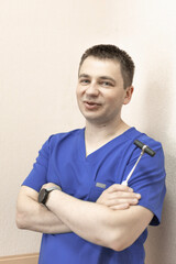a male doctor stands against the wall and holds a reflex nerve tapping instrument in his hand
