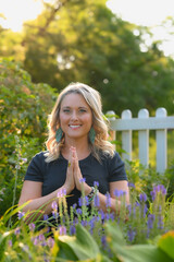Woman in prayer position doing yoga in a park. White picket fence background. 
