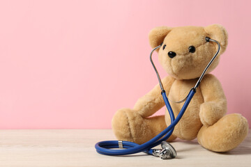 Pediatrics concept. Teddy bear with stethoscope on wooden table against pink background, space for...