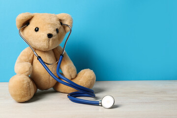 Pediatrics concept. Teddy bear with stethoscope on wooden table against light blue background,...