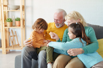 Senior Couple Enjoying Quality Family Time With Young Grandchildren In Bright Living Room Setting