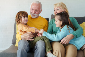 Caucasian Grandparents Sharing Joyful Moments with Grandchildren on a Comfortable Sofa in a Bright...
