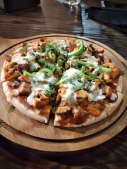 Delicious thin crust pizza topped with chicken or paneer, green bell peppers, and melted mozzarella, served on a wooden board. Perfectly baked with a rich tomato base.