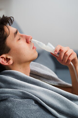 Young man with asthma attack breathing with inhaler in the bad. Doing nose inhalation with...
