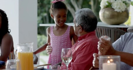 Elderly couple enjoying outdoor diverse family dinner, smiling and engaging in conversation, at home