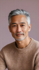 Obraz premium Serene Reflection: An older Asian man, his silver hair and tranquil gaze reflecting a lifetime of experience, stands confidently in front of a soft pastel backdrop, conveying quiet wisdom and calm.