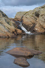 A serene photo of a small waterfall flowing between rocky cliffs into a calm pool.