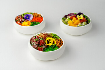 Fresh Poke Bowl Concept: three bowls with tuna, salmon, veggie and edible flowers, delicious healthy balanced meal
