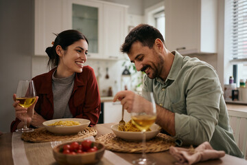 Happy couple eating pasta and communicating at dining table.
