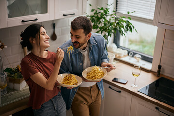 Carefree couple eating spaghetti in the kitchen.