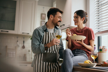 Happy couple talking while eating pasta and drinking wine at home.