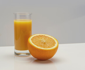 glass of orange juice and half of a large orange on white glass, copy space