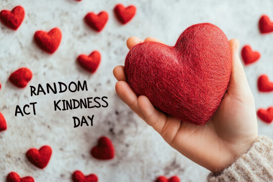 A child's hand holding a red heart surrounded by smaller hearts with random act of kindness day text