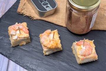 Prawn canape on black slate tray on wooden table with jars and cans of preserves