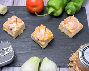 Prawn canape on black slate tray on wooden table with jars, cans of preserves, peppers, onion and tomato