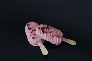 Two pink ice cream sticks with red sprinkles on top. The sticks are placed on a black background
