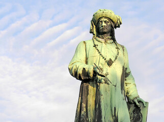 bronze statue of jan van eyck, flemish painter in bruges, belgium with white clouds. Selective focus
