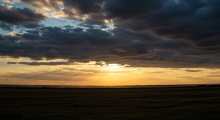 Fototapeta premium Golden Sunset Over Prairie - Dramatic sunset over a vast prairie landscape with dark clouds and golden light