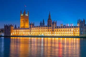 Westminster Palace stands majestically beside the River Thames, bathed in warm lights against a...
