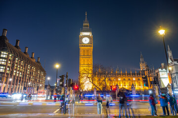 As night falls over London, crowds gather near Big Ben and Westminster Palace. Traffic flows...
