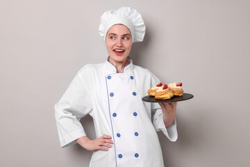 Confectioner in uniform holding delicious profiteroles on light grey background