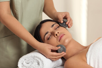 Young woman receiving facial massage with spa stones in salon