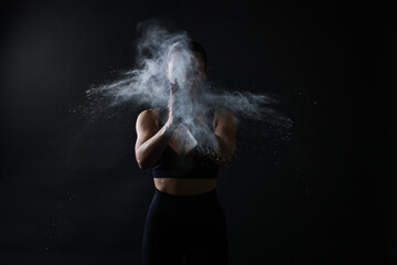 Woman clapping hands with talcum powder before training on black background