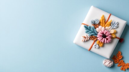 A beautifully wrapped gift box adorned with intricate floral embroidery, placed on a soft blue background, and elegant and minimalistic composition.