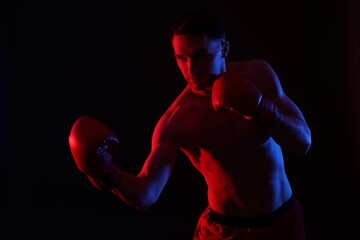 Man in boxing gloves fighting on black background in neon lights