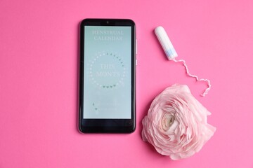 Smartphone with period calendar application, tampon and flower on pink background, flat lay
